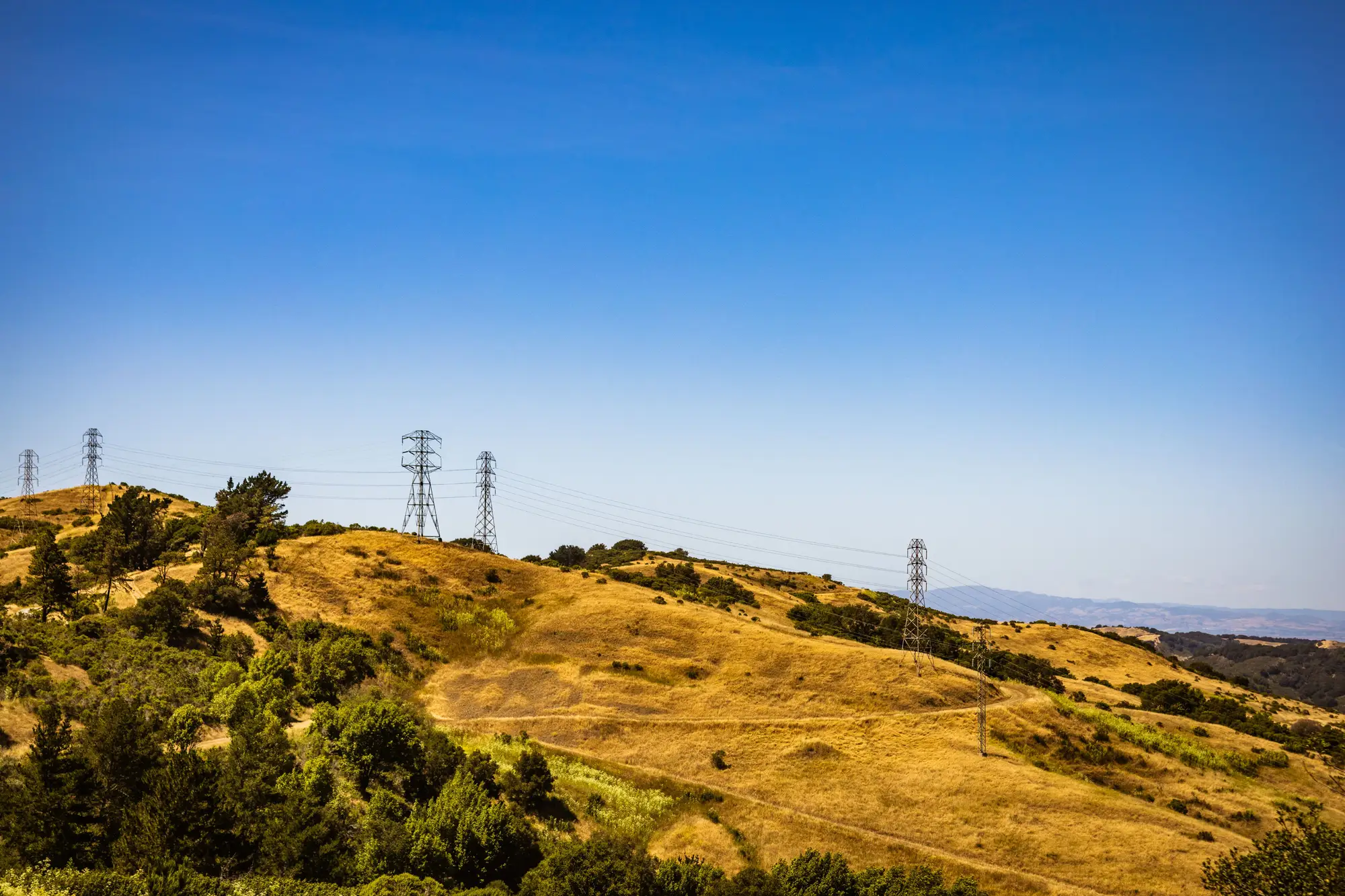 Transmission towers running over dry rolling hills under a clear sky