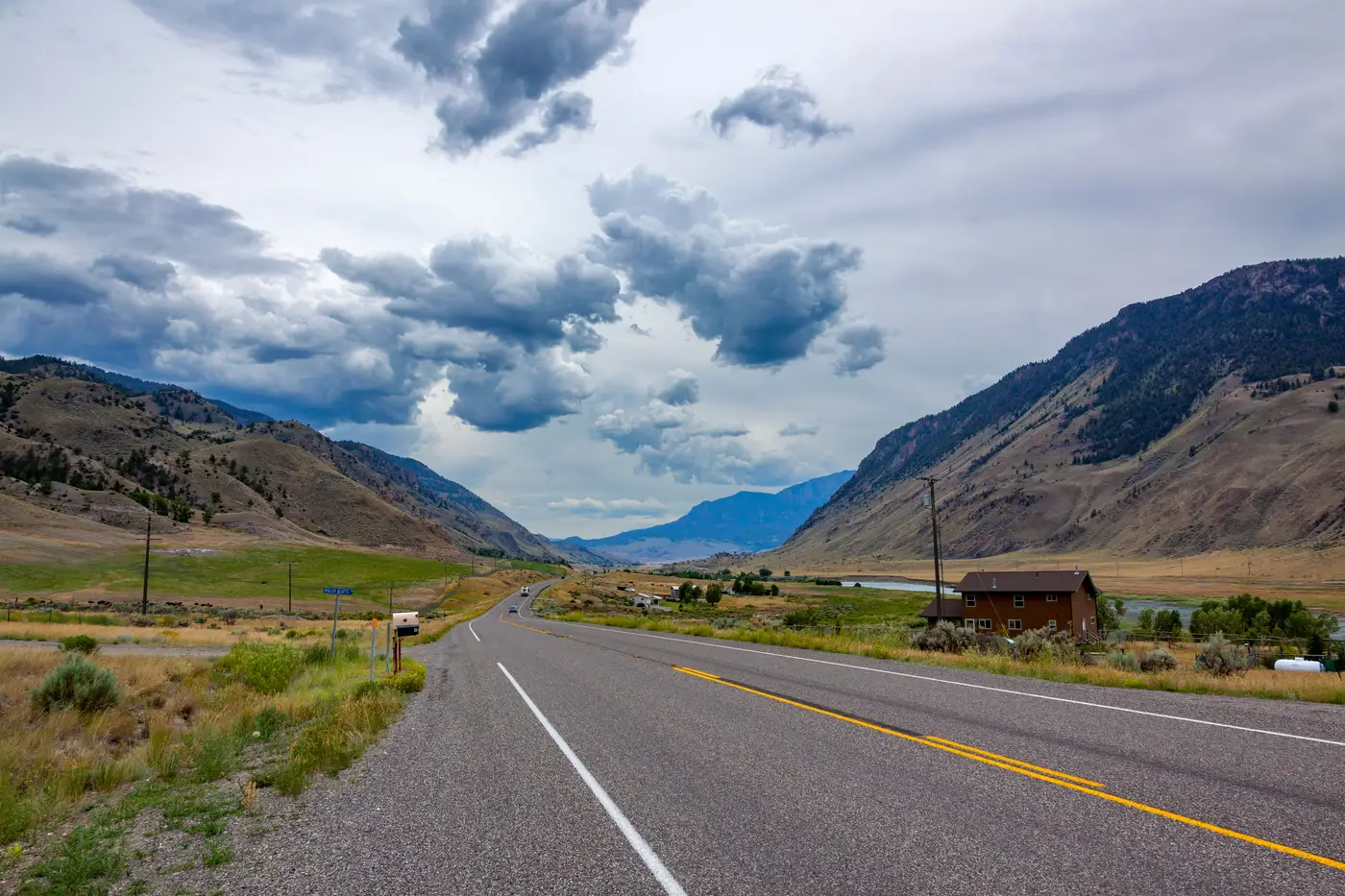 A two-lane highway running through a mountain valley, steep slopes rising on both sides under a clouded sky.